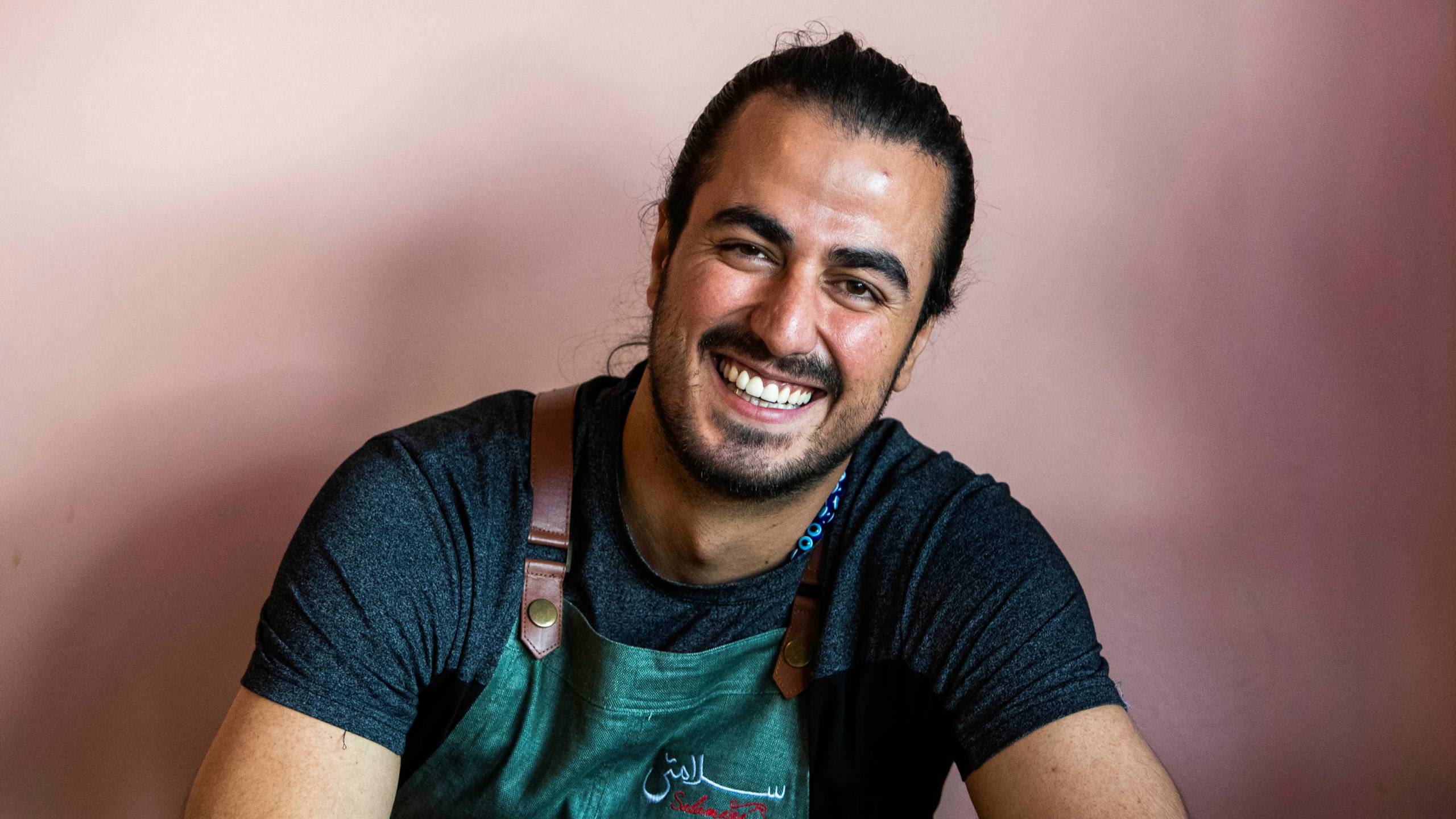 Hamed Allahyari in a Salamatea House apron against a pink wall